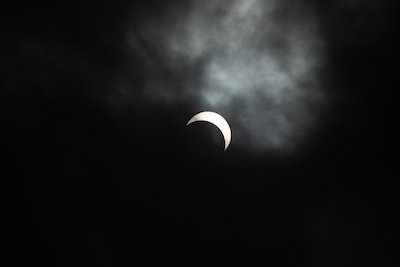 Sliver of crescent moon shining brightly with clouds floating by