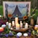 Outdoor Beltane altar with lit candles, flowers, and artwork
